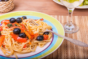 Vegetarian pasta with vegetables, linguine with bell pepper, tomatoes and olives on a plate standing on a napkin on the table and a glass of dry white wine, close-up