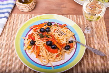 Vegetarian pasta with vegetables, linguine with bell pepper, tomatoes and olives on a plate standing on a napkin on the table and a glass of dry white wine, close-up