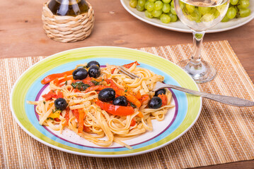 Vegetarian pasta with vegetables, linguine with bell pepper, tomatoes and olives on a plate standing on a napkin on the table and a glass of dry white wine, close-up