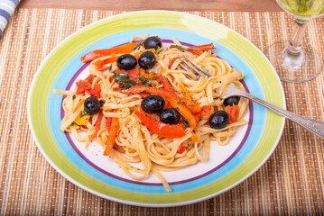 Classic Italian pasta with vegetables, linguine with sweet peppers, tomatoes and olives on a plate on a napkin on the table, close-up