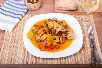 Chicken in Roman style with sweet pepper in a plate and a glass of dry white wine - close-up, top view