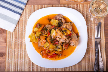 Italian chicken stew - chicken in Roman style with sweet pepper in a plate and a glass of dry white wine - close-up, top view