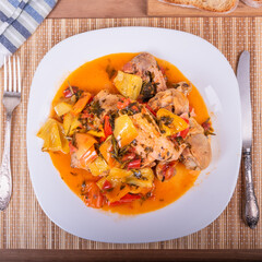 Chicken with bell peppers in a plate on a napkin with cutlery - classic Italian recipe, close-up, top view