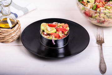 Italian Tuscan panzanella salad, mixed salad of bread and vegetables in a culinary ring on a black plate and a glass bowl with ready-made salad on a wooden light table, close-up
