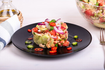 Italian tuscan salad panzanella, mixed salad of bread and vegetables on a black plate decorated with chilli peppers and a glass bowl with ready-made salad on a wooden light table, close-up
