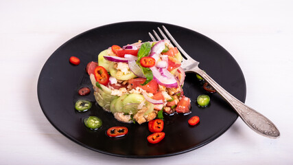 Italian tuscan vegetarian panzanella salad, mixed bread and vegetable salad on a black plate decorated with chilli peppers on a wooden light table, close-up