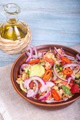 Italian tuscan vegetarian panzanella salad, mixed salad of breads, tomatoes and vegetables in a clay bowl on a linen napkin and a jug of olive oil on a wooden table