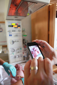 Father Holding Cell Phone Taking Picture of His Newborn At Hospital