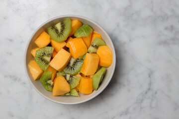 Fruit bowl with kiwi and peach on a marble table. Top view