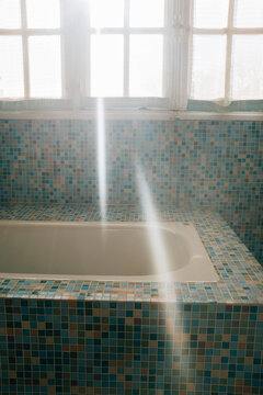 Sunlight shining into bathroom and onto tiled bathtub, Provence, France