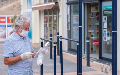 Fototapeta na wymiar Senior man white haired wearing medical mask and protective gloves to prevent coronavirus infection goes to pharmacy - new normal concept