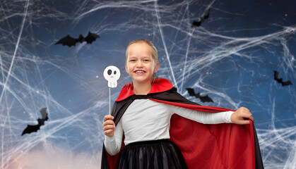 halloween, holiday and childhood concept - girl in dracula costume with black cape holding scull...