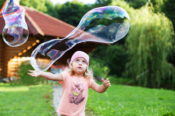 happy girl playing with soap bubbles outdoor. A little girl pops a soap bubble