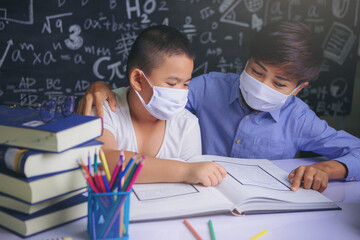 Young female teacher with face mask explaining and teaching schoolboy for lesson in a book at school classroom