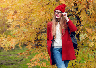 Smiling blonde  woman with long hairs walking in sunny  autumn park in trendy casual outfit.