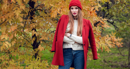 Autumn fashion  portrait of  blonde woman in red stylish coat and knitted hat  walking in park.