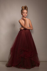 Fototapeta premium Beautiful little girl child in a ball gown with evening hairstyle in the studio on a gray background