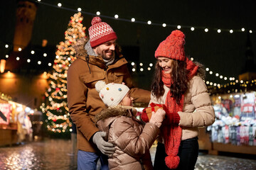 family, winter holidays and celebration concept - happy mother, father and little daughter with gift at christmas market on town hall square in tallinn, estonia