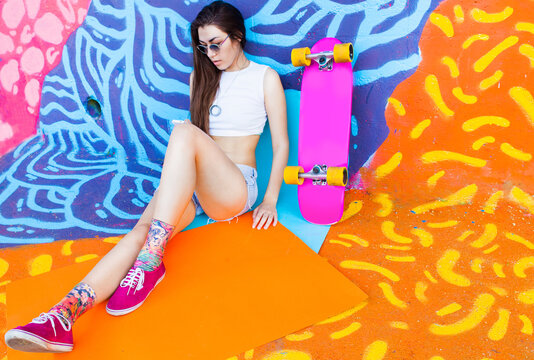 Attractive urban skategirl sitting in front of colorful background