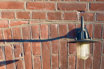 Classic steel lamp hanging of a red brick wall in daytime.