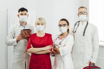 A team of four doctors in protective medical masks stand in line at the clinic. The work of doctors during a coronavirus pandemic. Young doctors in masks, self-safety