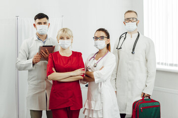 A team of doctors in protective masks during a coronavirus pandemic going to visit the patient. Portrait of young doctors standing in a row. Work of physicians during the quarantine of coronavirus - Powered by Adobe