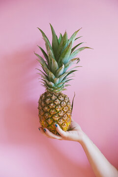 Woman holding a pineapple in front of the pink background