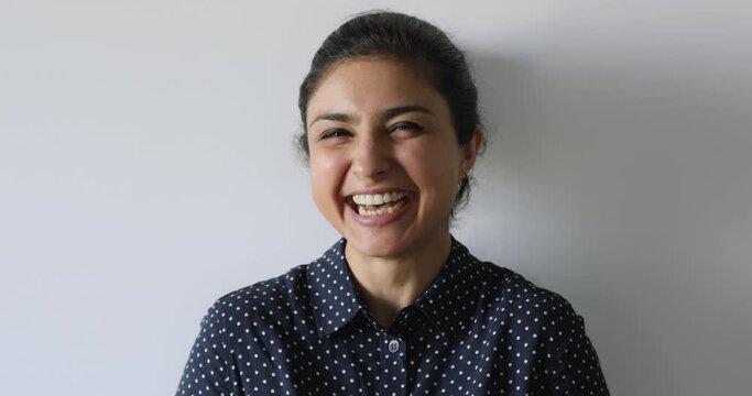 Head shot on grey studio background posing Indian ethnicity 30s woman laughing over joke having positive mood feels rejoice untroubled female indoor, close up. Happy millennial girl portrait concept