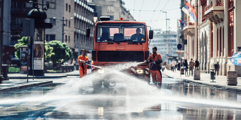 two street-sweeping workers using a hose to clean off litter, street sweepe