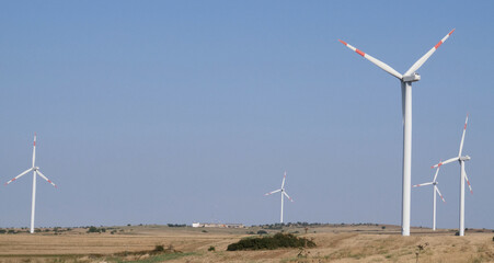 Wind turbines on beautiful sunny summer autumn of the hills of Apuliia (murgia). Curvy road through Eolic park. Green ecological power energy generation. Wind farm eco field