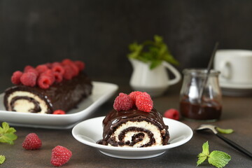 Chocolate roll with cream cheese and raspberries, with a cup of coffee on a dark background.