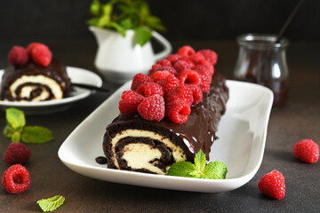 Chocolate roll with cream cheese and raspberries, with a cup of coffee on a dark background.