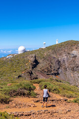 A young woman walking next to the telescopes of the Roque de los Muchachos National Park on top of...