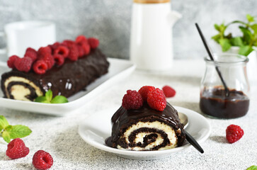 Biscuit roll with chocolate and raspberries on a light concrete background.