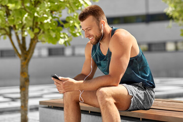 Fototapeta na wymiar fitness, sport and technology concept - young athlete man with earphones and smartphone listening to music outdoors