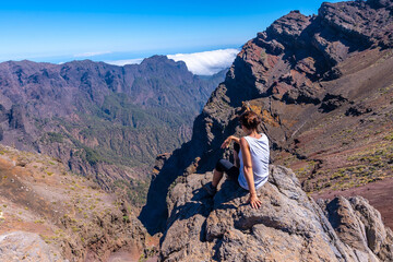 A young woman sits resting and looking at the views of the Roque de los Muchachos national park on top of the Caldera de Taburiente, La Palma, Canary Islands. Spain