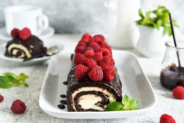 Biscuit roll with chocolate and raspberries on a light concrete background.