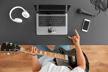 leisure, music and people concept - young man or musician with laptop computer playing guitar...