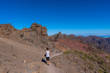 Fototapeta premium A young woman walking atop the Caldera de Taburiente volcano near Roque de los Muchachos one summer afternoon, La Palma, Canary Islands. Spain