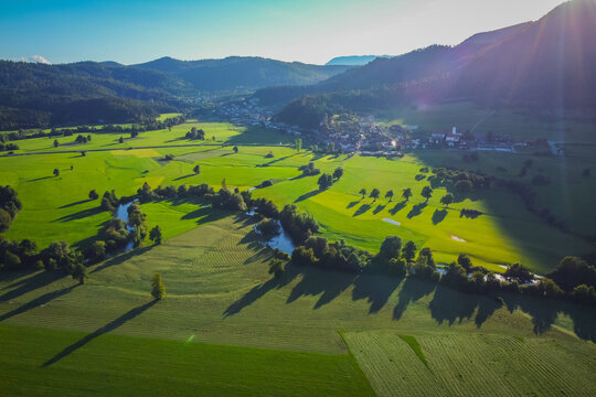 Aerial view of Unica or Unec river on Planinsko polje field in the late summer. Green fields and forests seen from above. Behind a village of Planina is visible.
