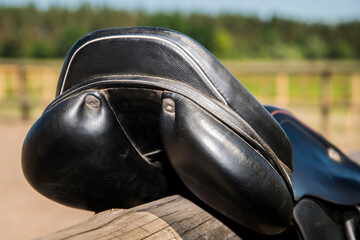 Black leather saddle on a wooden fence.