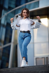 A beautiful girl in blue jeans and a white t-shirt runs down the stairs. Portrait of a running girl in a white jacket.