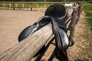 Wooden rural fence with black horse saddle.