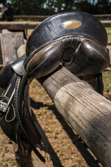 Old used black leather saddle on a wooden fence.