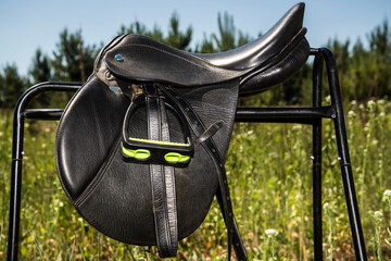 Black leather saddle for horse on a metal platform.
