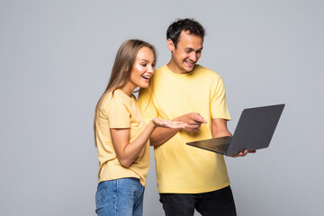 Portrait of a happy young couple using laptop computer while standing over gray wall background