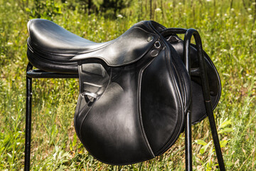 Close-up view of black horse saddle against green grass background.