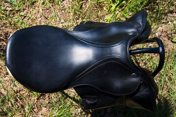 Top view of black horse saddle against ground background.