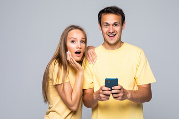 Young couple having smart phones in hands, looking at screen, surprised, using 5g internet, standing over grey background