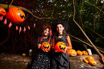 Portrait of two girls in costumes holding toy pumpkins and smiling at camera they are at the party in the dark